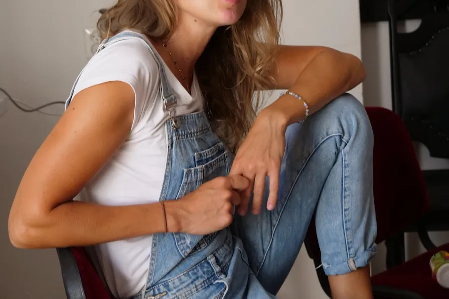 Zdjęcie przedstawia próbę stolikową do spektaklu „Ifigenia ze Splott”. Na krześle z jedną zgiętą nogą pod sobą siedzi bokiem Agnieszka Skrzypczak. Druga noga, również jest zgięta i łokieć aktorki jest na niej oparty. Drugi łokieć spoczywa na oparciu krzesła. Postawa Agnieszki Skrzypczak jest lekko zgarbiona a jej usta lekko otwarte. 