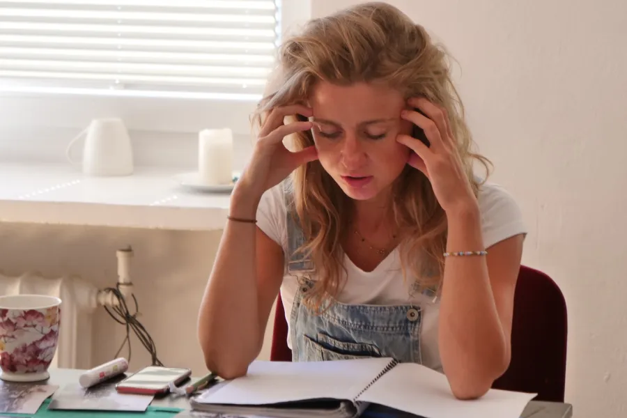 Zdjęcie przedstawia próbę stolikową do spektaklu „Ifigenia ze Splott”. Z łokciami na stole siedzi intensywnie myśląca Agnieszka Skrzypczak. Palce obydwu dłoni aktorki dotykają jej skroni. Jej oczy są zamknięte a usta lekko otwarte. Na stole, nad którym pochyla się aktorka znajduje się zeszyt, długopis, telefon, kubek w kwiaty i czarno-białe zdjęcia.