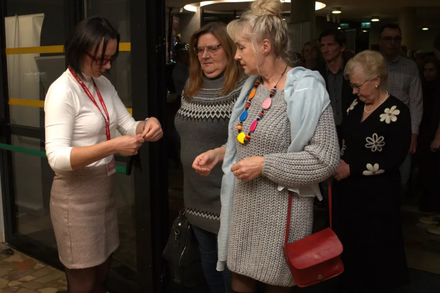 zdjęcie przedstawia grupę osób oczekujących na sprawdzenie biletów przed wejściem na salę teatralną