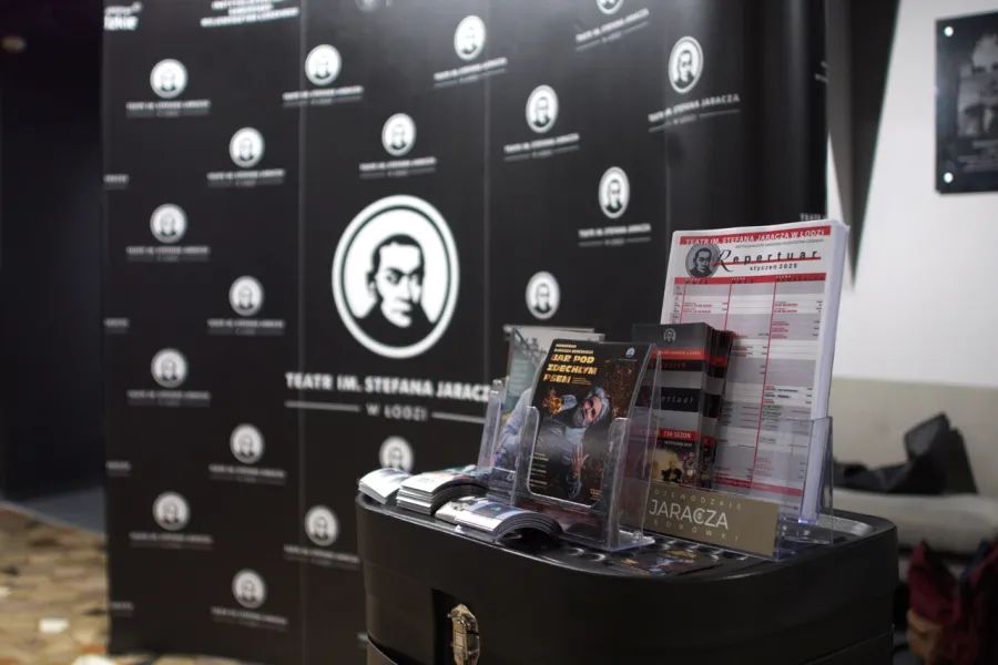 Zdjęcie przedstawia ściankę reklamową Teatru Jaracza w Łodzi i materiały promocyjne 