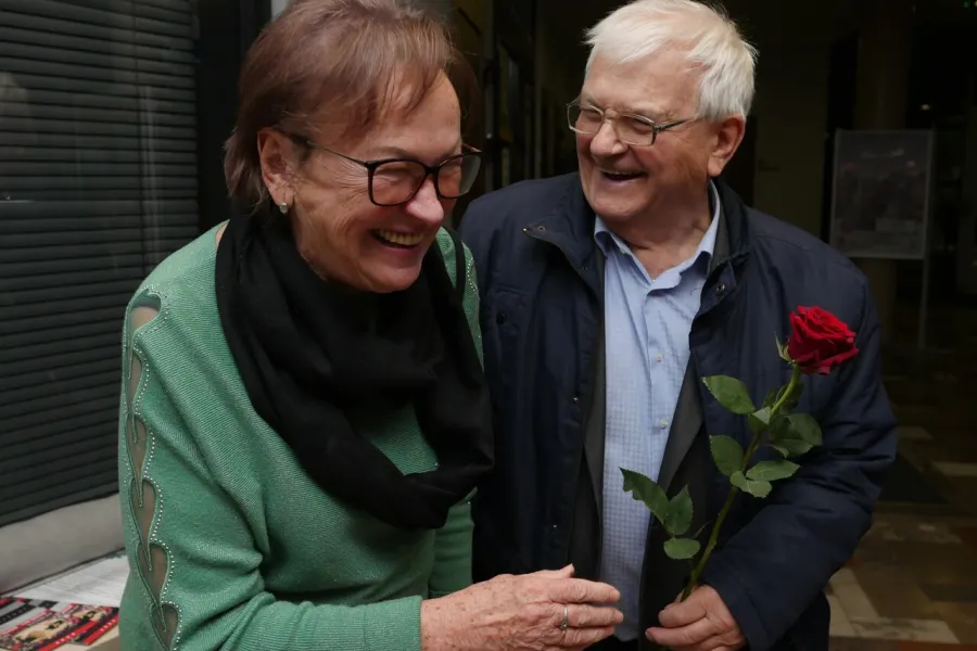 Zdjęcie przedstawia dwójkę starszych uśmiechniętych ludzi - kobietę i mężczyznę. Mężczyzna trzyma w ręku czerwoną różę. 