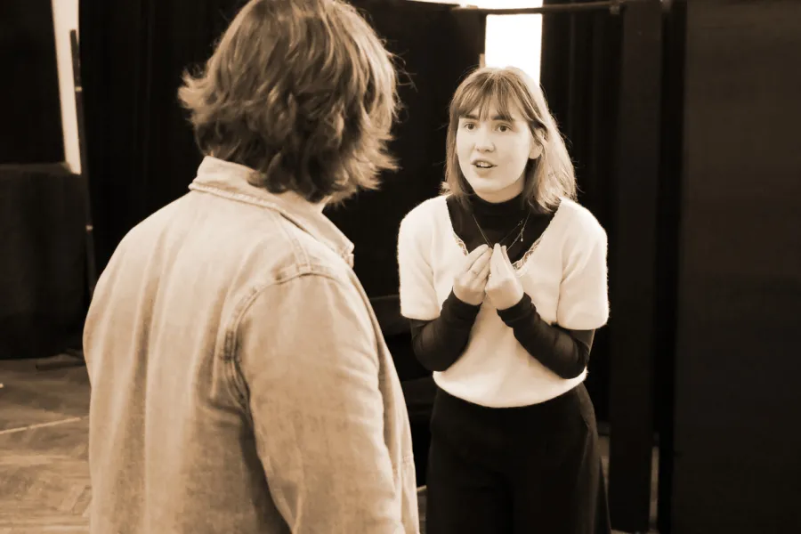 zdjęcie przedstawia dwójkę aktorów na sali prób. Jeden z aktorów, Konrad Krupiński, stoi tyłem do obiektywu. Aktorka, Szantal Strzelińska, ma ręce złożone w błagalnym geście. 