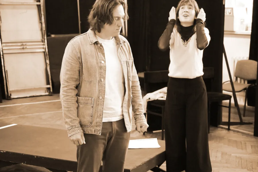 zdjęcie przedstawia dwójkę aktorów. Aktor Konrad Krupiński ma zaciśnięte pięści, aktorka Szantal Strzelińska sto i za nim z rękoma przy twarzy. 