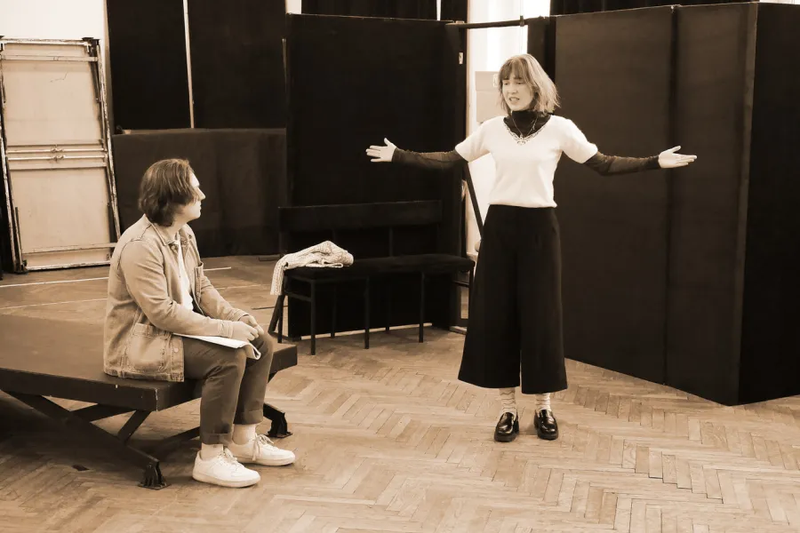 zdjęcie przedstawia dwójkę aktorów. Konrad Krupiński siedzi na podeście, Szantal Strzelińska stoi obok z rozłożonymi rękoma. 