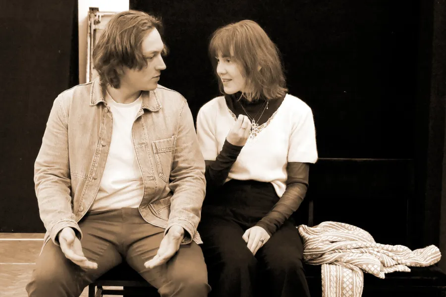 Zdjęcie przedstawia dwójkę aktorów siedzących na podeście. 