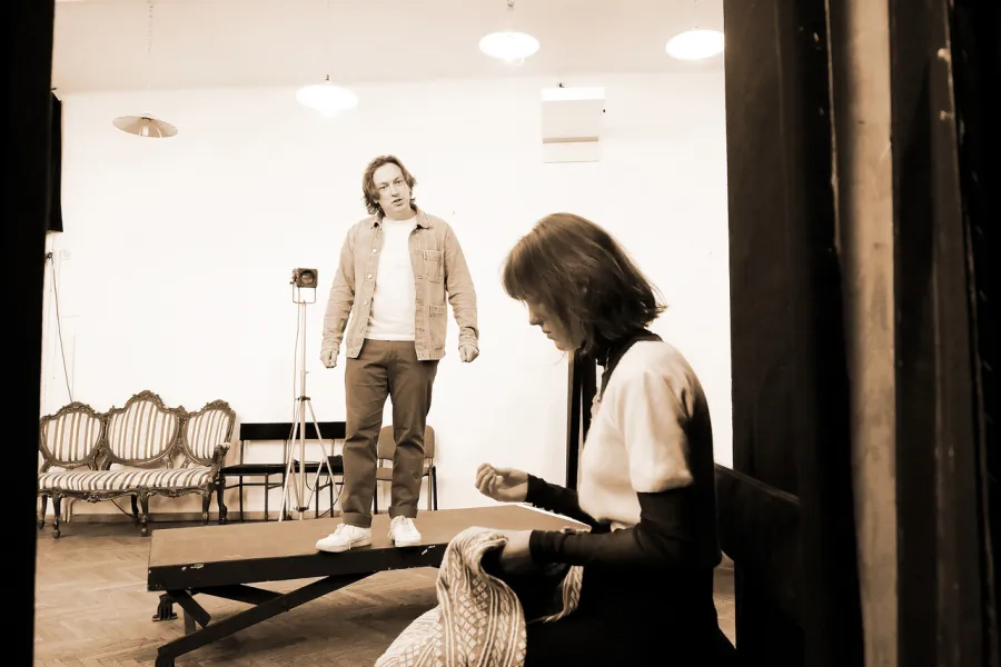 zdjęcie przedstawia dwójkę aktorów. Aktor stoi na podeście, na pierwszym planie bokiem stoi aktorka. 