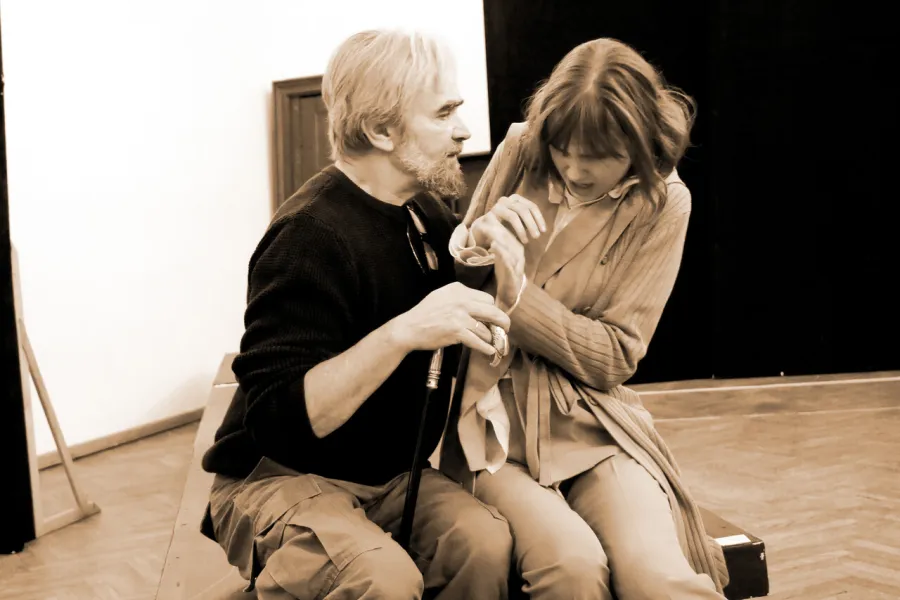 zdjęcie przestawia dwoje aktorów: Dariusza Bereskiego i Szantal Strzelińską siedzących na podeście w sali prób. Aktorka odpycha od siebie aktora. 