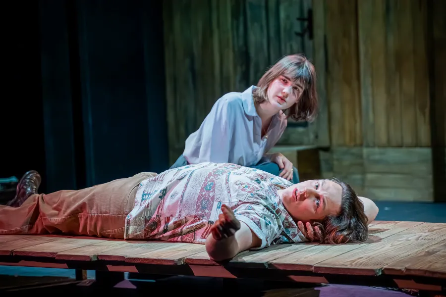 zdjęcie przedstawia dwójkę aktorów. Aktor Konrad Krupiński leży na drewnianym pomoście i patrzy w stronę obiektywu. Aktorka siedzi nad nim. 