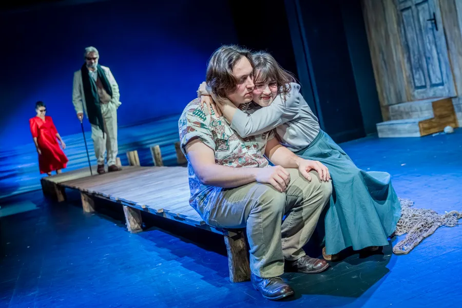 na zdjęciu dwójka aktorów Konrad Krupiński i Szantal Strzelińska siedzą na drewnianym pomoście przytuleni. W tle widać idącego po pomoście aktora Dariusza Bereskiego i wchodzącą na pomost Ewę Audykowską-Wiśniewską 