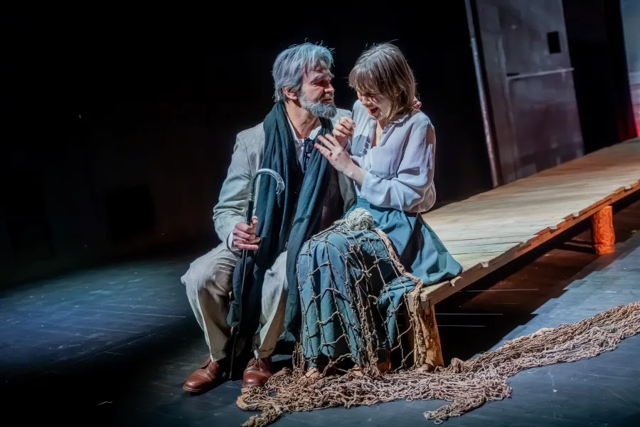 na zdjęciu dwoje aktorów Dariusz Bereski i Szantal Strzelińska siedzą na drewnianym pomoście. Dariusz Bereski zbliża się mocno do aktorki, ona go odpycha z grymasem na twarzy.