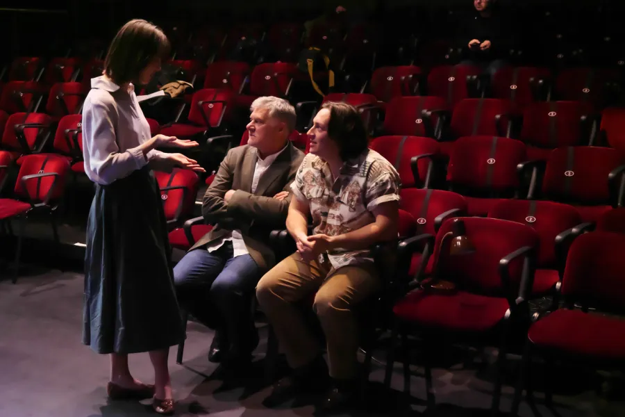 Zdjęcie z próby medialnej spektaklu „Zamiana". Zdjęcie zostało wykonane na Scenie Kameralnej. Widać widownię, przed krzesłem stoi aktorka Szantal Strzelińska, na dwóch krzesłach siedzą od lewej reżyser spktaklu Marek Pasieczny i Konrad Krupiński. 