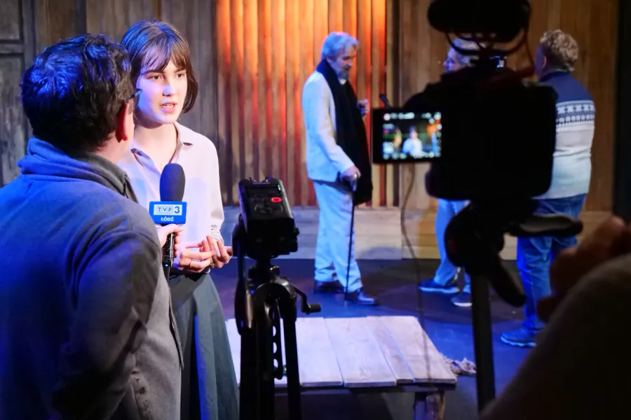 Zdjęcie z próby medialnej spektaklu „Zamiana". Zdjęcie wykonane na Scenie Kameralnej, w dekoracji spektaklu. Na pierwszym planie widać aktorkę Szantal Strzelińską udzielającą wywiadu dla TVP 3 Łódź. W tle widać aktora Dariusza Bereskiego, udzielającego wywiadu innym mediom. 