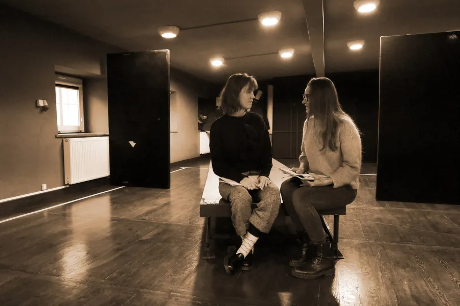 Zdjęcie z próby spektaklu „Zamiana". Dwie aktorki siedzą na podeście. W rękach trzymają scenariusze. 