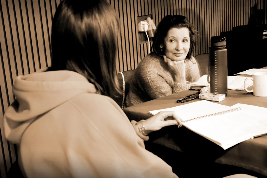 Zdjęcie z prób do spektaklu „Zamiana". Aktorka siedzi za stołem, na którym leżą scenariusze sztuki. Tyłem na drugim krześle siedzi inspicjentka.