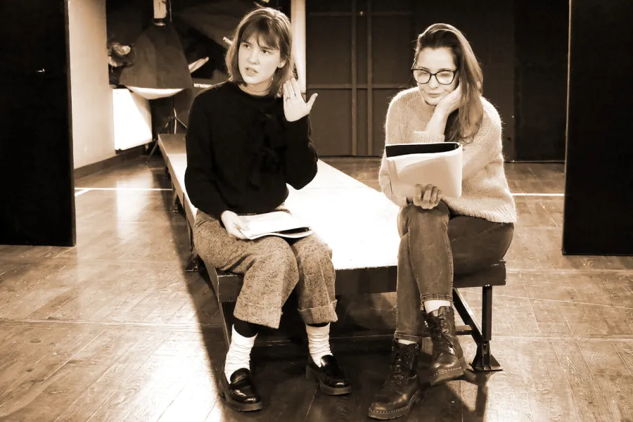 Zdjęcie z próby spektaklu „Zamiana". Dwie aktorki siedzą na podeście. W rękach trzymają scenariusze. 