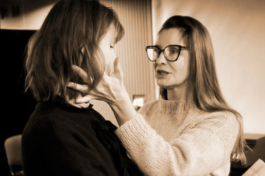 Zdjęcie z próby do spektaklu „Zamiana". Na zdjęciu widać dwie aktorki. Jedna jest zwrócona bokiem do obiektywu, druga trzyma ręce na jej policzkach. 