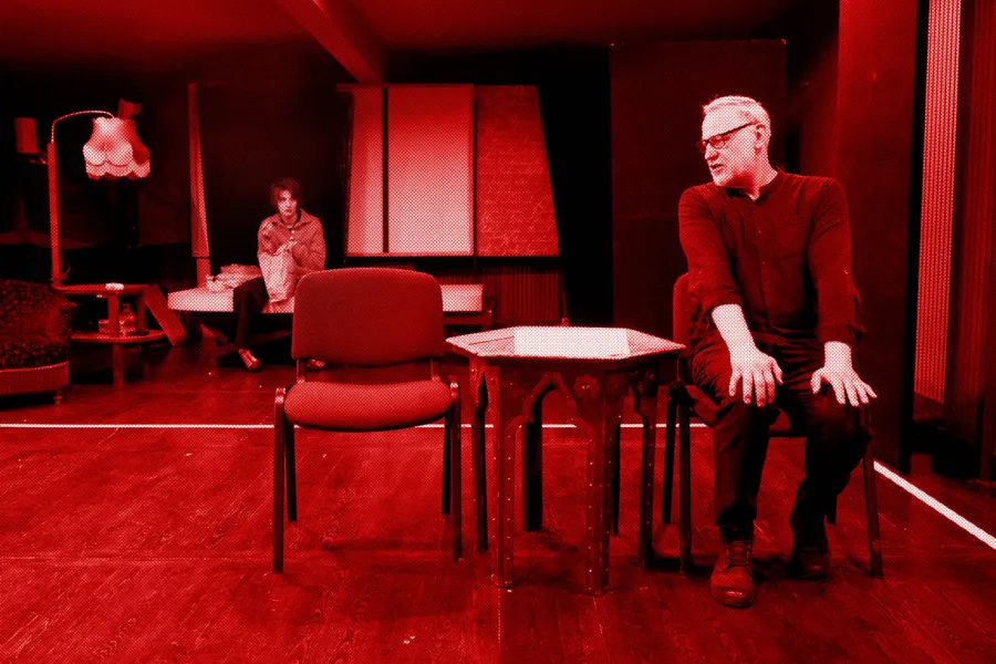 próba do spektaklu „Morderstwo w hotelu", zdjęcie zostało zrobione w sali prób, na zdjęciu: siedząca na łóżku i jedząca z papierowej torby Natalia Klepacka oraz siedzący na krześle przy niskim stoliku i patrzący na Natalię przez prawe ramię Mariusz Witkowski, fot. Marcin Nowak. Na zdjęcie został nałożony czerwony filtr.