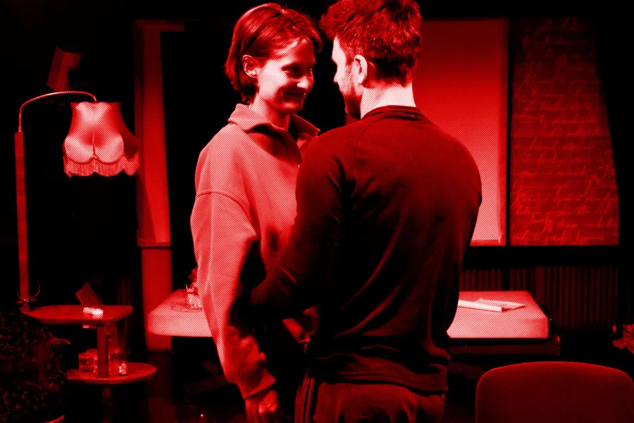 próba do spektaklu „Morderstwo w hotelu", zdjęcie zostało zrobione na sali prób,na zdjęciu: Natalia Klepacka, Krzysztof Wach. Aktorzy stoją blisko siebie, twarzami zwróconymi do siebie, obejmując się, fot. Marcin Nowak. Na zdjęcie nałożony jest czerowny filtr. 