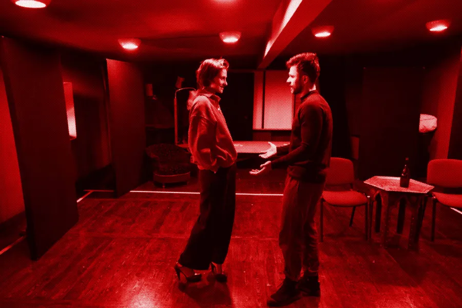 próba do spektaklu „Morderstwo w hotelu", zdjęcie zostało zrobione w sali prób,na zdjęciu: Natalia Klepacka, Krzysztof Wach. Aktorzy stoją od siebie w odległości, twarzami zwróconymi do siebie, trzymają się za ręce, fot. Marcin Nowak. Na zdjęcie nałożony jest czerowny filtr. 