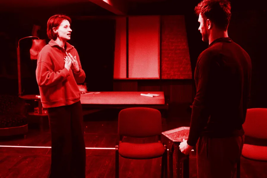 próba do spektaklu „Morderstwo w hotelu", zdjęcie zostało zrobione w sali prób,na zdjęciu: Natalia Klepacka, Krzysztof Wach. Aktorzy stoją od siebie w odległości, twarzami zwróconymi do siebie. Natalia Klepacka ma przyciągnięte do klatki piersiowej ręce, fot. Marcin Nowak. Na zdjęcie nałożony jest czerowny filtr. 