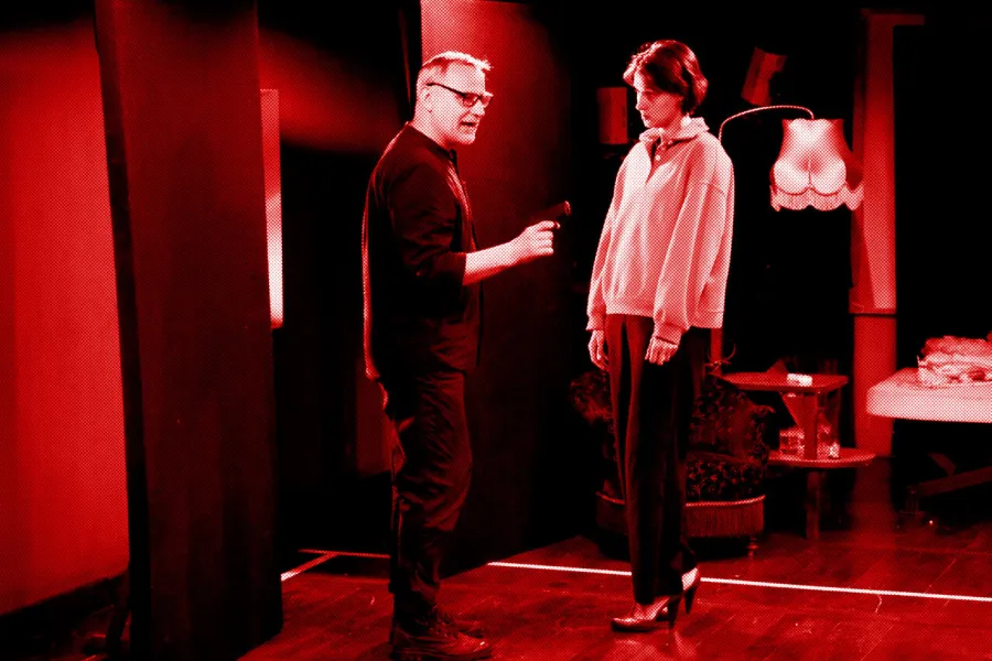 próba do spektaklu „Morderstwo w hotelu", zdjęcie zostało zrobione w sali prób, na zdjęciu: Mariusz Witkowski trzymający w ręku pistolet i Natalia Klepacka, fot. Marcin Nowak. Na zdjęcie nałożony jest czerwony filtr.