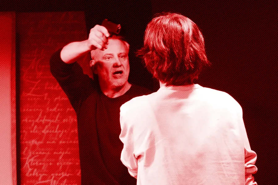 próba spektaklu „Morderstwo w hotelu", na zdjęciu Mariusz Witkowski celujący z pistoletu w Natalię Klepacką, fot. Macin Nowak. Na zdjęcie został nałożony czerwony filtr.