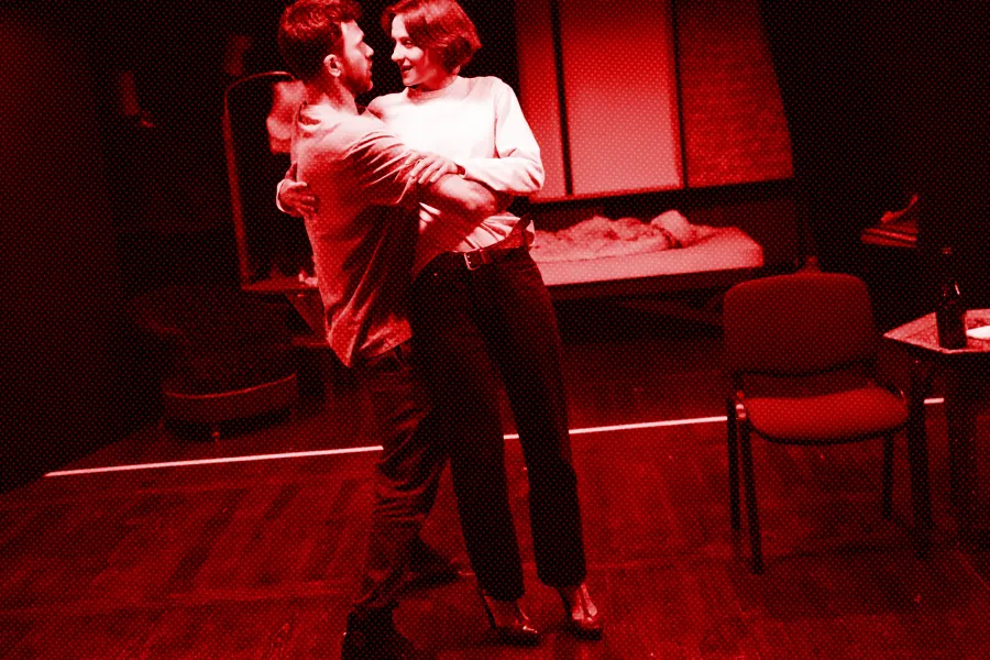 próba spektaklu „Morderstwo w hotelu",  zdjęcie zostało zrobione na sali prób, na zdjęciu Krzysztof Wach, Natalia Klepacka. Aktorzy obejmują się. fot. Macin Nowak. Na zdjęcie nałożony jest czerwony filtr.