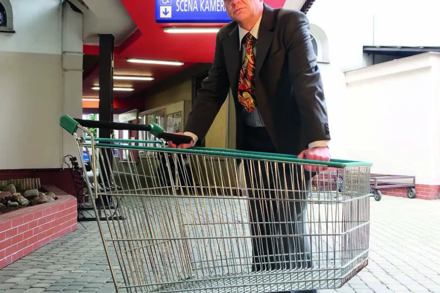 sesja zdjęciowa do spektaklu, na zdjęciu: Mariusz Witkowski stoi nad wózkiem sklepowym z pistoletem w ręku. Zdjęcie zrobione jest na podwórku, w przejściu na Scenę Kameralną. Na aktorem widnieje tablica podświetlana z napisem Scena Kameralna, fot. Marcin Nowak