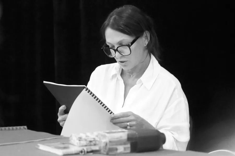 pierwsza próba spektaklu „Czas na wielki numer", na zdjęciu aktorka Monika Badowska, która siedzi przy stole i czyta egzemplarz sztuki, naz djęcie nałożony jest czarno-biały filtr, fot. Marcin Nowak