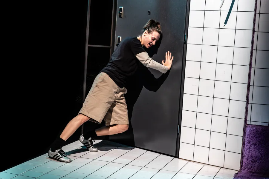 Zdjęcie ze spektaklu „Czas na wielki numer". Na fotografii widać aktorkę Natalię Klepacką, która blokuje ciałem drzwi wejściowe uniemożliwiając wejście osoby z zewnątrz. Jest o nie oparta lewym barkiem i przytrzymuje drzwi prawą ręką. Autorką fotografii jest Natalia Kabanow.