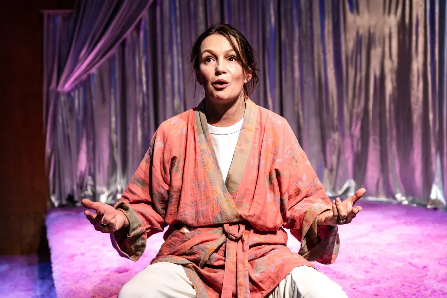 Zdjęcie ze spektaklu „Czas na wielki numer". Na fotografii aktorka Monika Badowska siedzi po turecku na scenie, ręce ma ułożone jak do medytacji. Na sobie ma kolorowy szlafrok. Autorką zdjęcia jest Natalia Kabanow. 